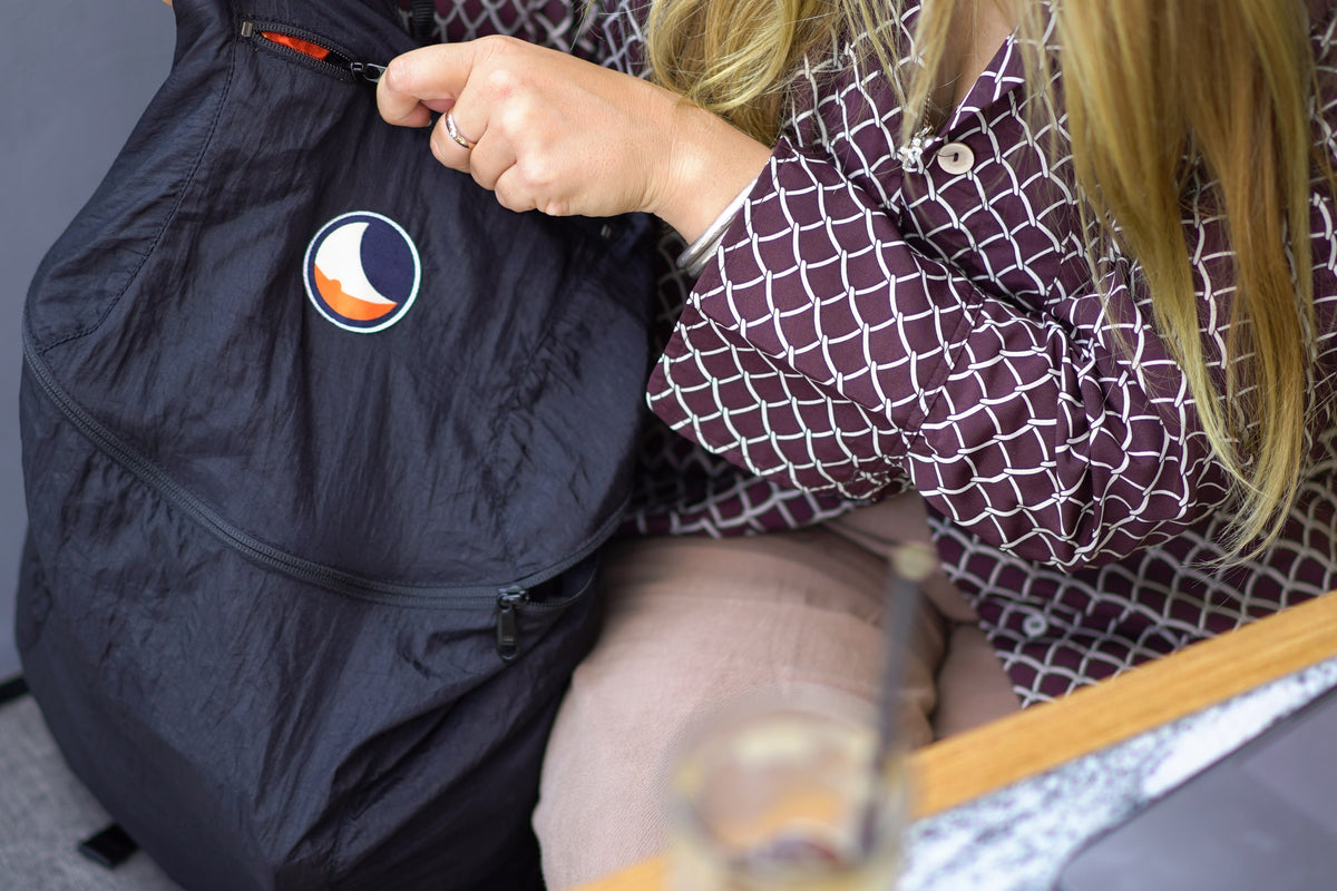 Woman unzipping the front pocket of a black Backpack Plus 25L