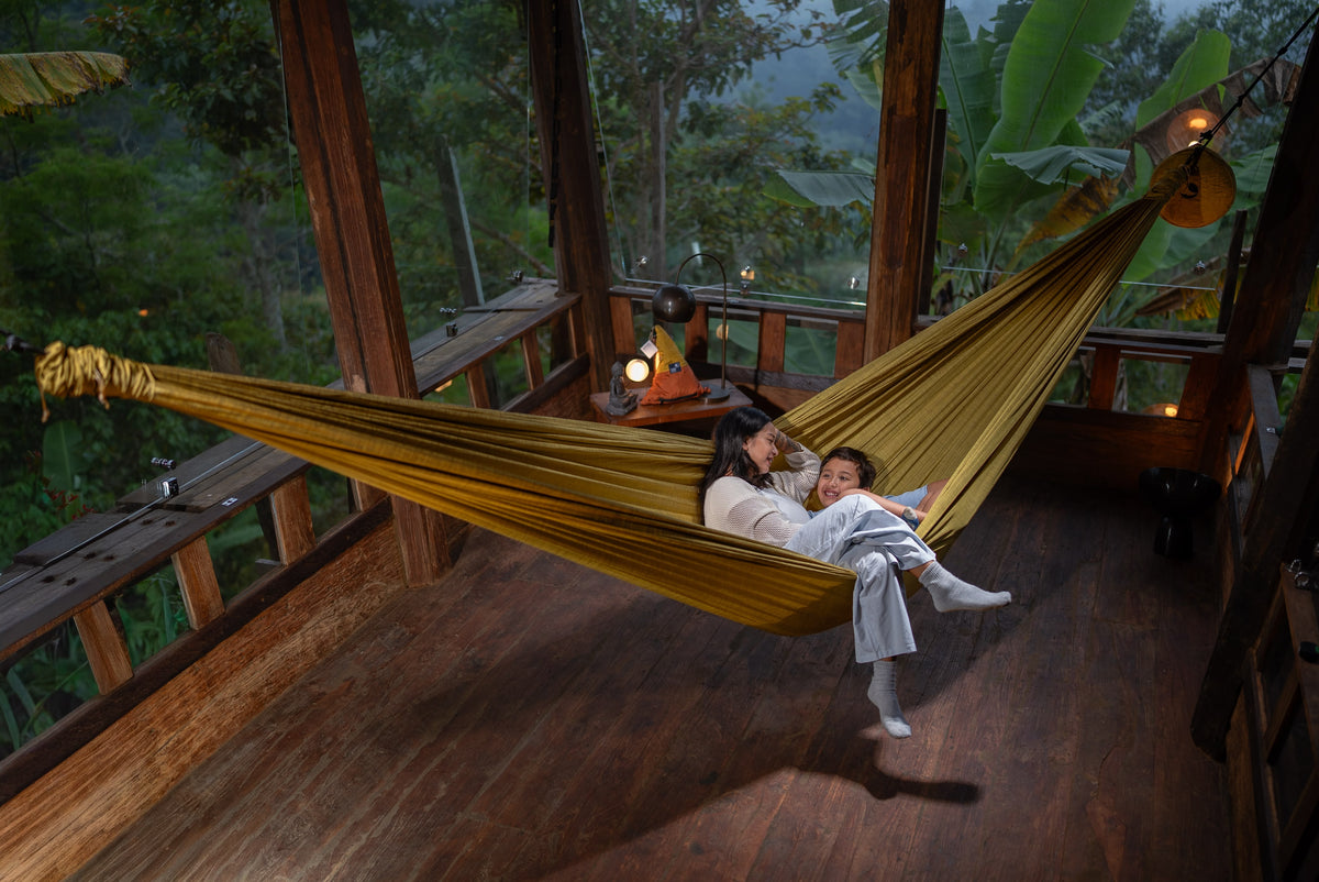 Mother and child relaxing in a golden Home Hammock 520 on a wooden deck surrounded by jungle