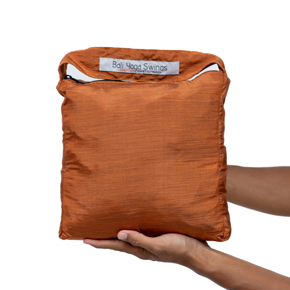 Hands holding the Yoga Hammock packed in its Terracotta Orange zip bag
