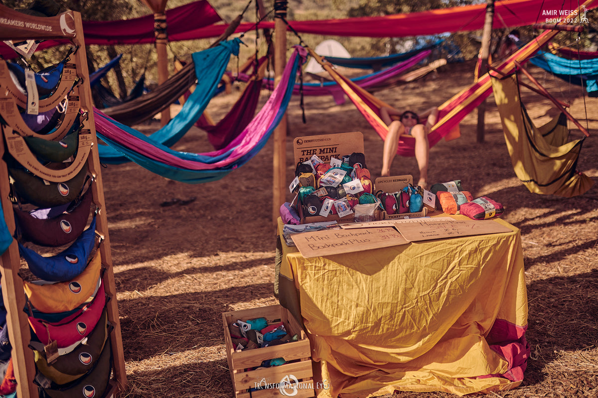Festival stall with colourful hammocks strung overhead, a rack of bum bags and a table of mini hammocks