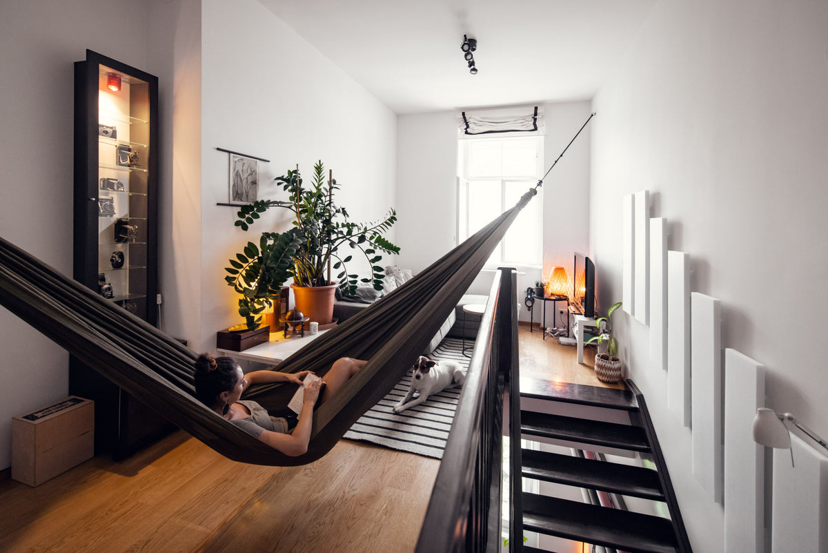 Woman reading in an Olive Brown Home Hammock 320 strung across a bright flat, with a dog lying below