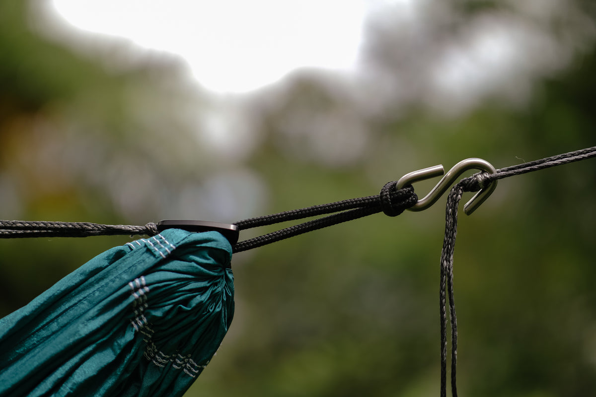 Close-up of a teal hammock end tied with black cord to a metal S-hook