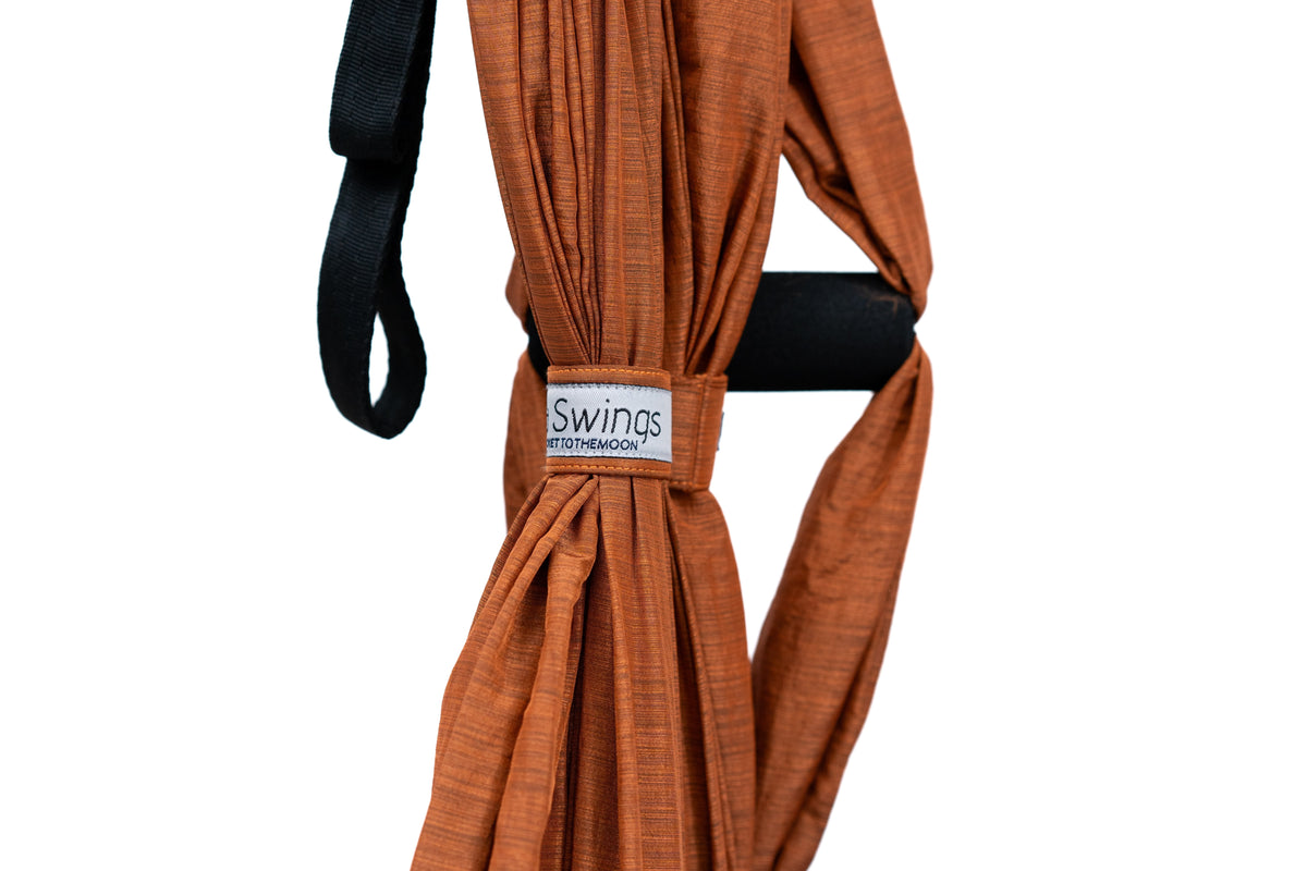 Close-up of the gathered Terracotta Orange Yoga Hammock fabric with its label, a padded foam handle and a black strap loop